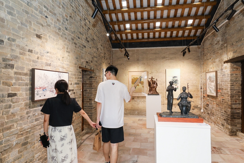 “晴耕雨读——青苗画家计划师生乡村艺术振兴作品展”在广州市花都区炭步镇塱头古村展出，图为情侣在参观作品展。受访者供图